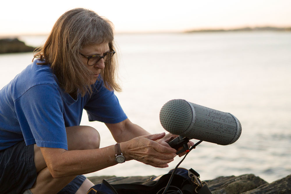 Dianne Ballon setting up mic on rocky coast at sundown