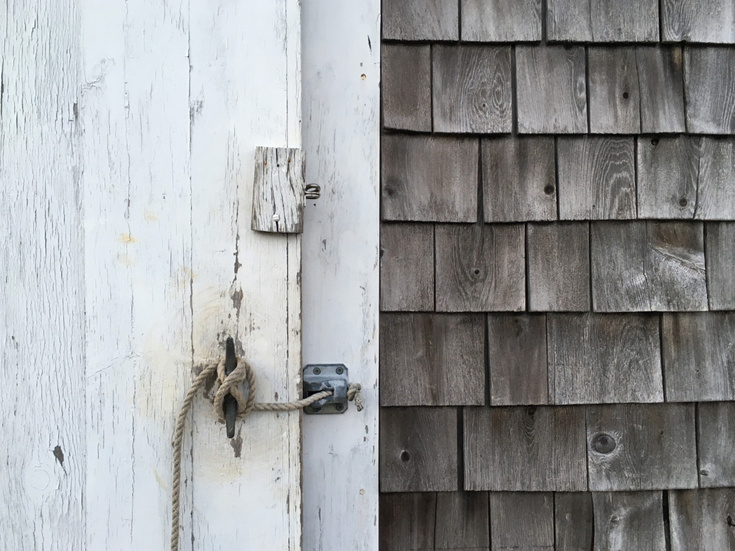 Weathered boathouse building closeup with rope and cleat to latch door.
